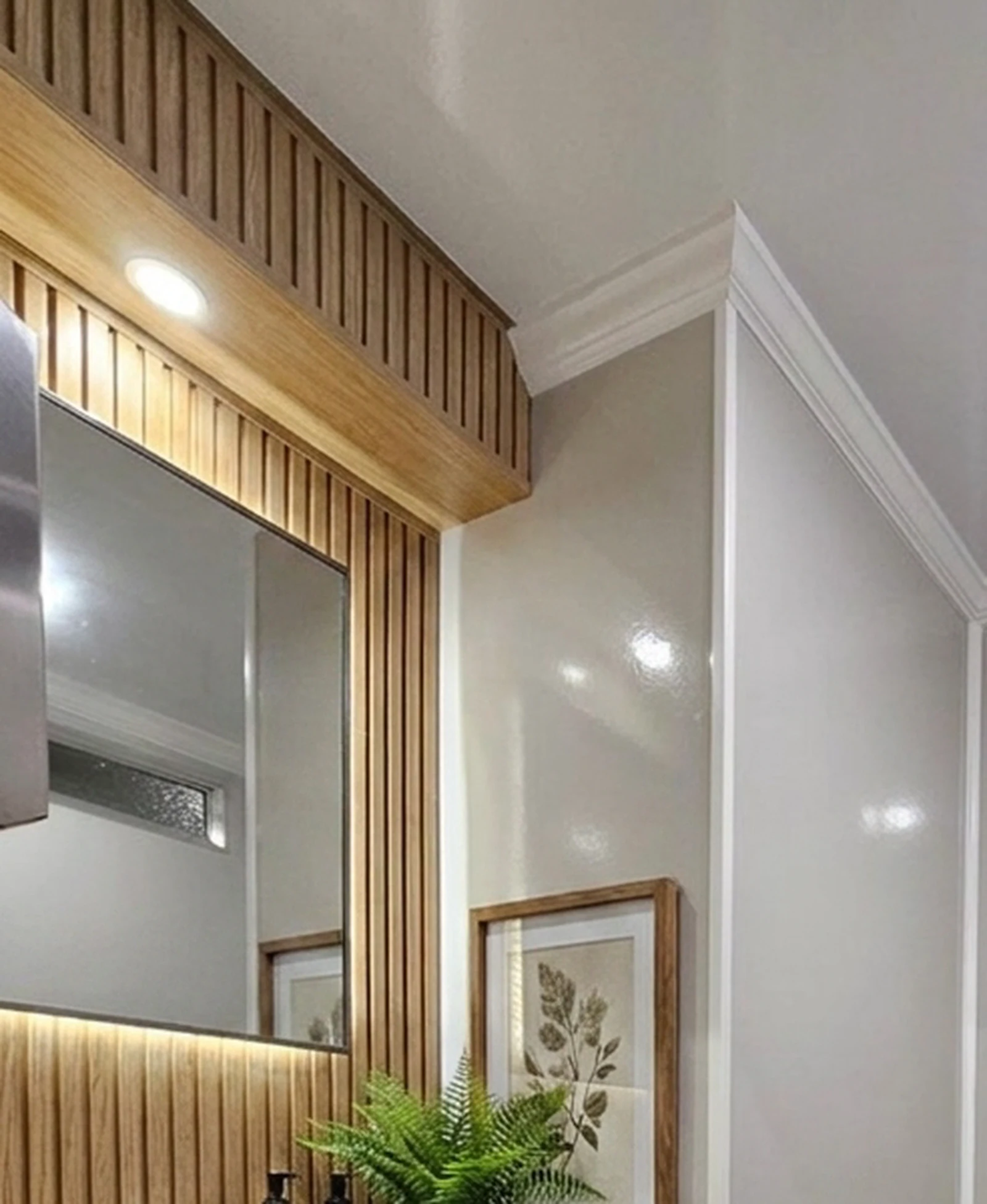 Backlit mirror framed in vertical wood slats with a botanical print beside it