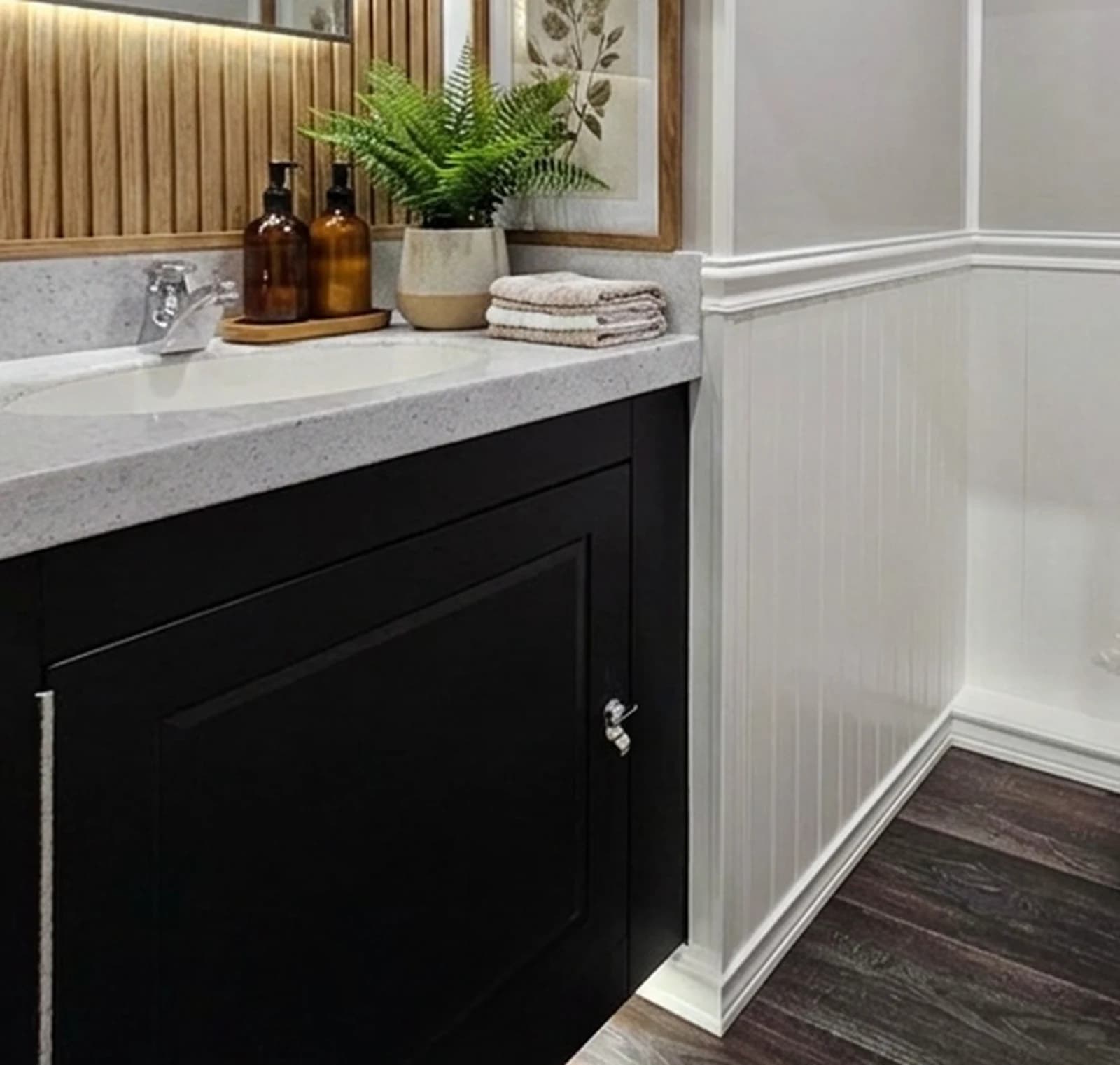 Vanity detail: speckled quartz countertop, potted fern, amber soap bottles on a wooden tray, folded towels